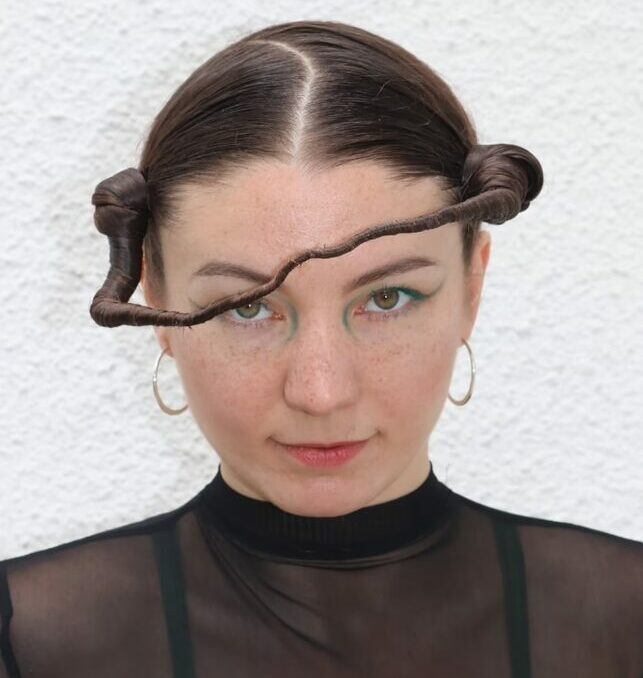 Natalia Gwiazdowska Responsible Fashion Business Na zdjęciu twarz kobiety z fryzurą przechodzącą przez część twarzy, połączone dwa koki i skrzywiony przedziałek. Kobieta ma kolczyki w kształcie kółek. Ubrana jest na czarno. fot. Natalia Celej